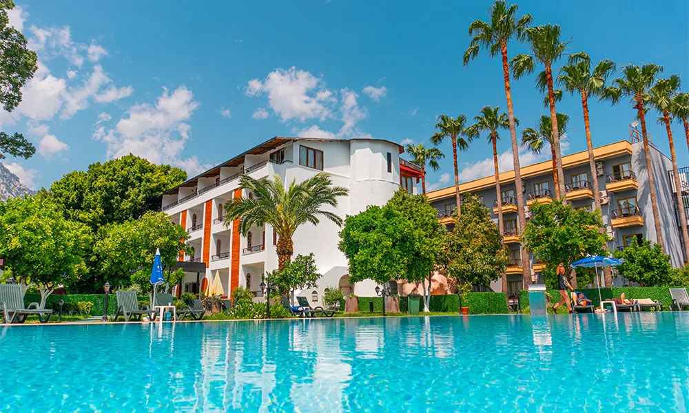 Palmiyeler ve otel binasıyla çevrili açık havuz
